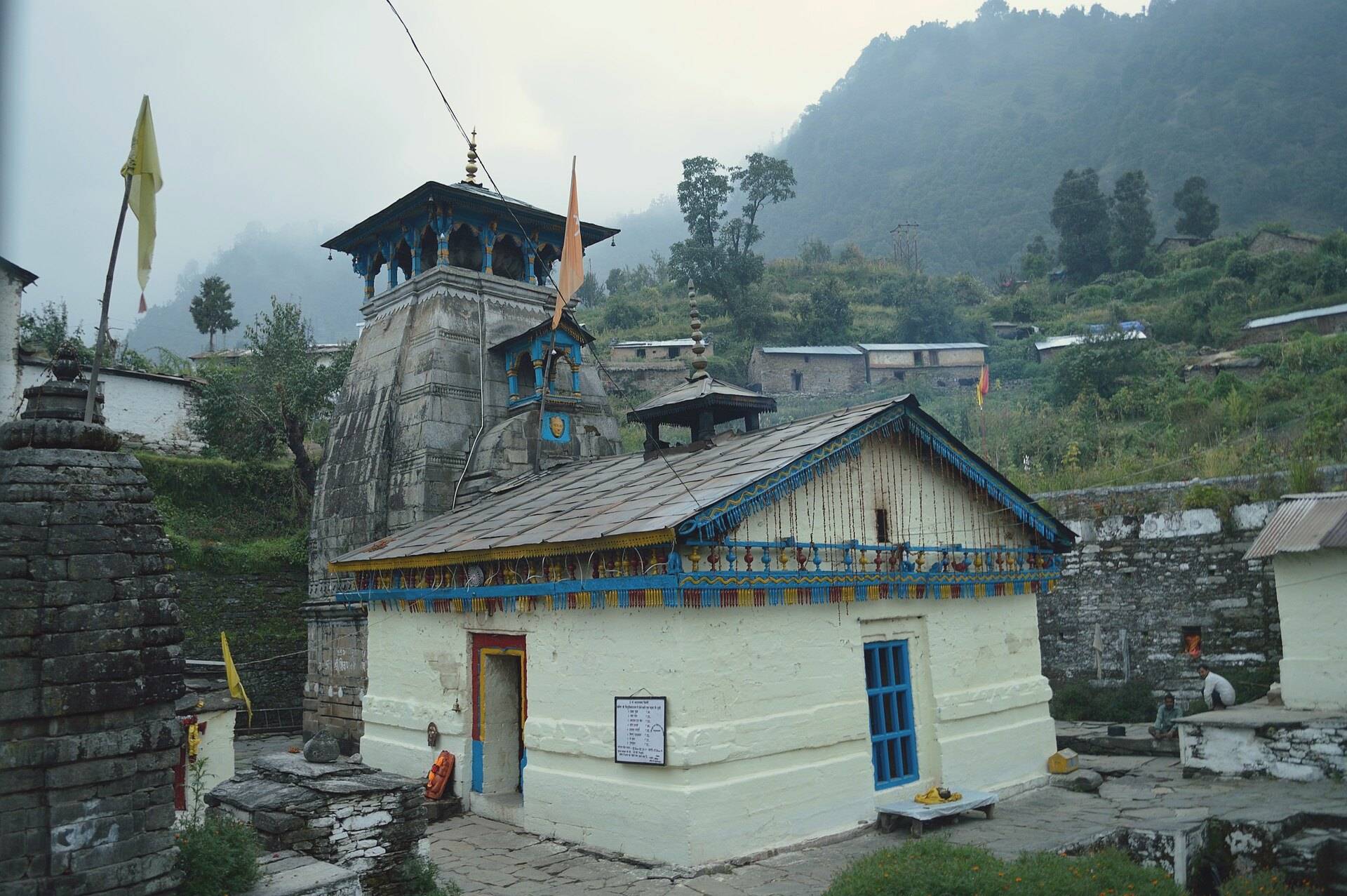 Triyuginarayan temple with forested hills and clouds behind it