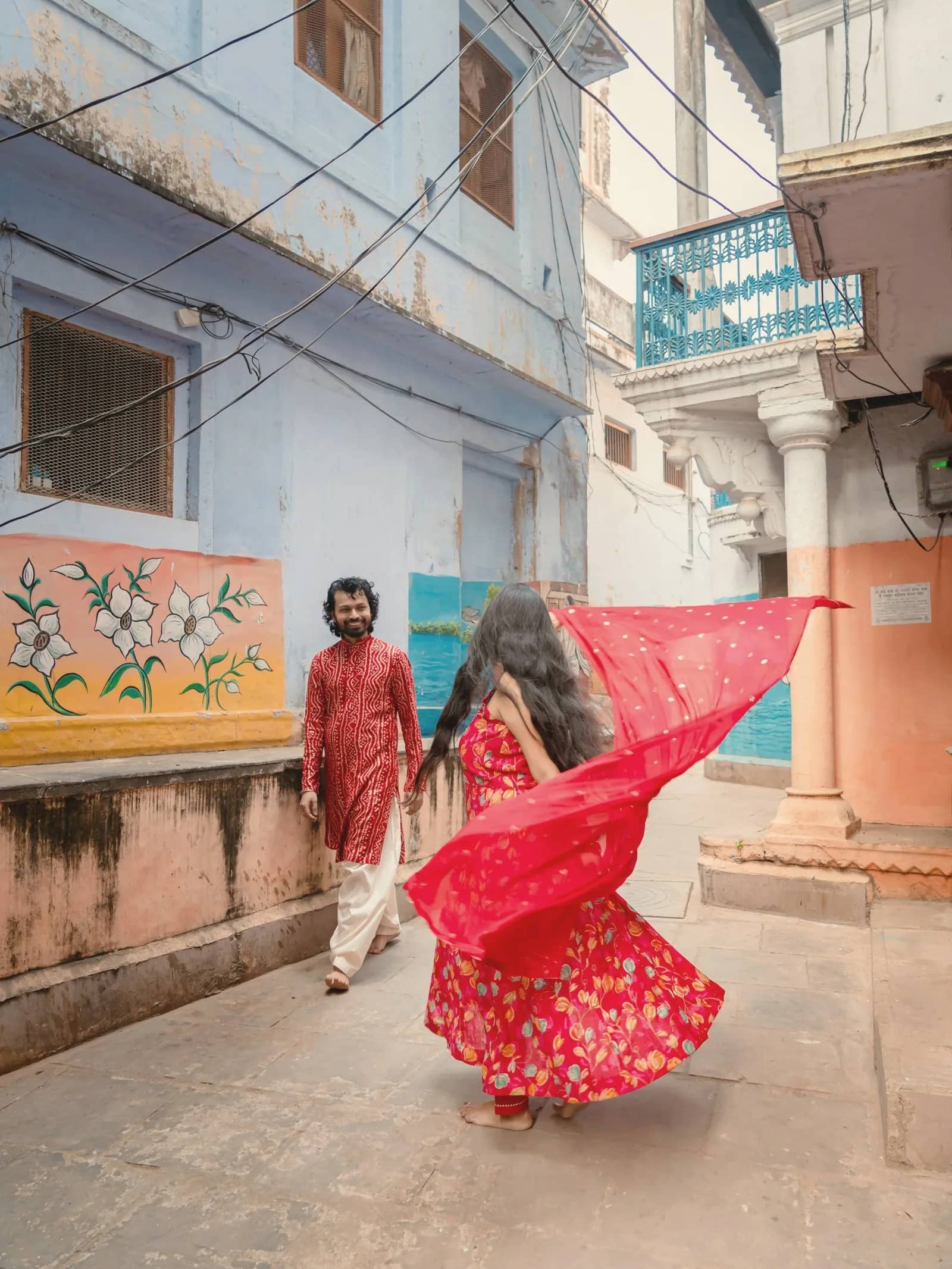 A couple walking through a colourful old street, her red dupatta flying