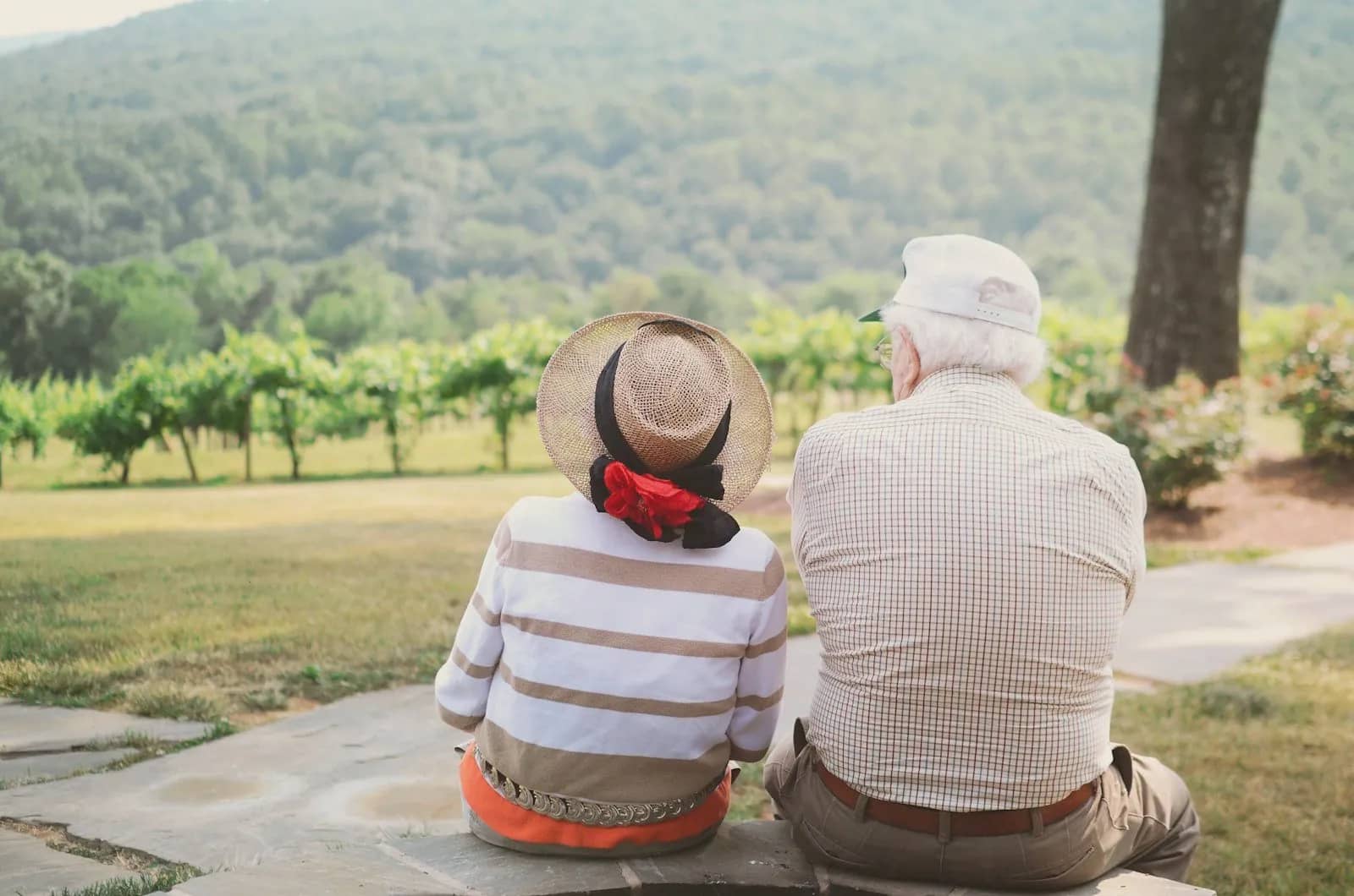 An older couple in sun hats sitting together looking at a green valley
